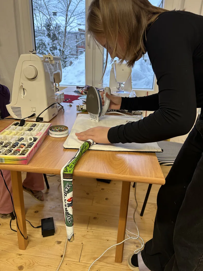 Ein Nähprojekt wird gebügelt, im Hintergrund Nähmaschinen und verschneite Bäume